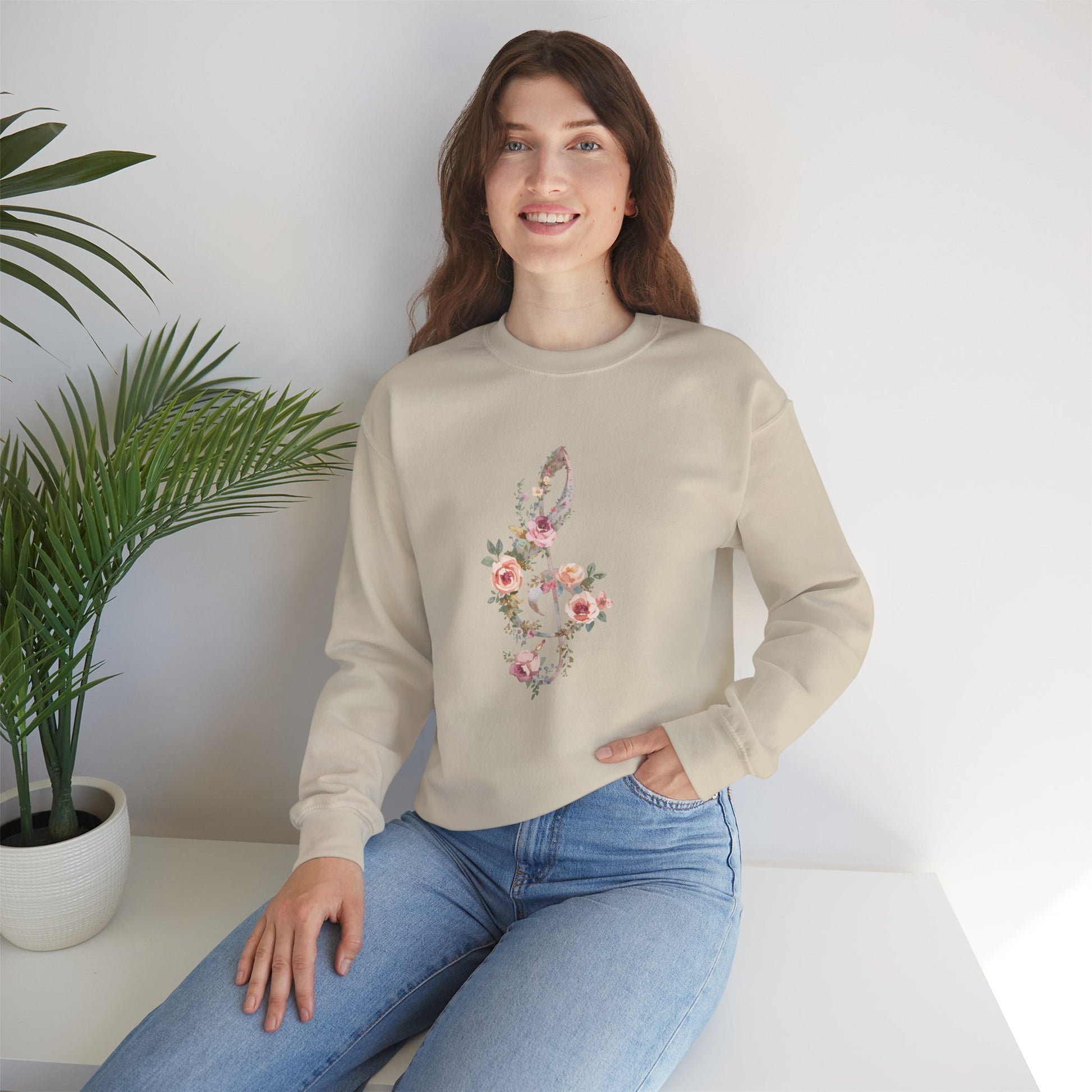 Woman wearing a beige sweatshirt with floral design sitting on a white surface with a plant in the background.